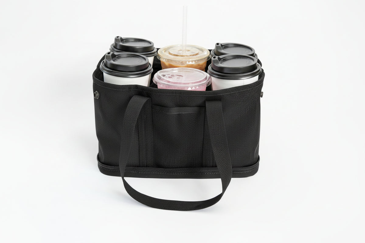 A black fabric carry bag with six compartments holding six reusable coffee cups with lids, photographed on a clean white background.