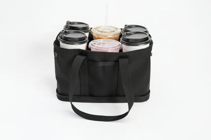 A black fabric carry bag with six compartments holding six reusable coffee cups with lids, photographed on a clean white background.